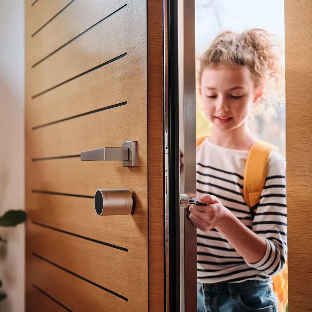 Enfant qui ouvre une porte d'entrée en bois avec une Clé Intelligente Netatmo, cylindre intérieur visible