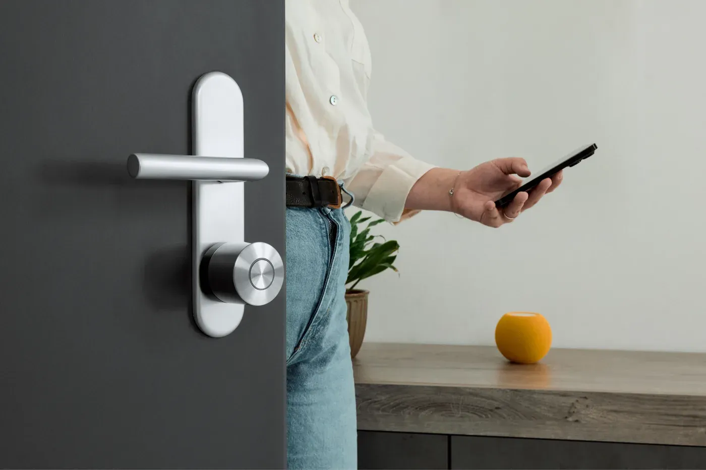 Une personne ouvre au téléphone une porte grise équipée d'une Nuki Smart Lock Ultra sous la poignée