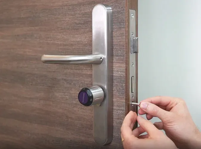 Une main visse le cylindre Waferlock C760 dans la têtière d'une porte en bois équipée d'une plaque inox